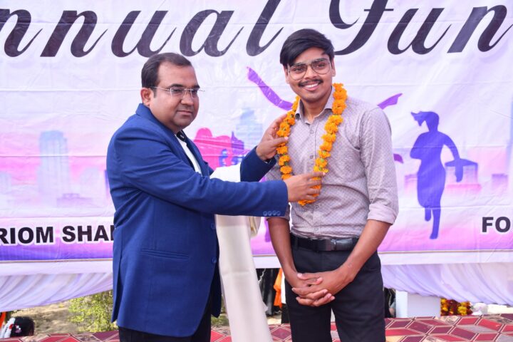 Principal Abhishek Srivastava placing a marigold garland around a young guest at the Annual Function.