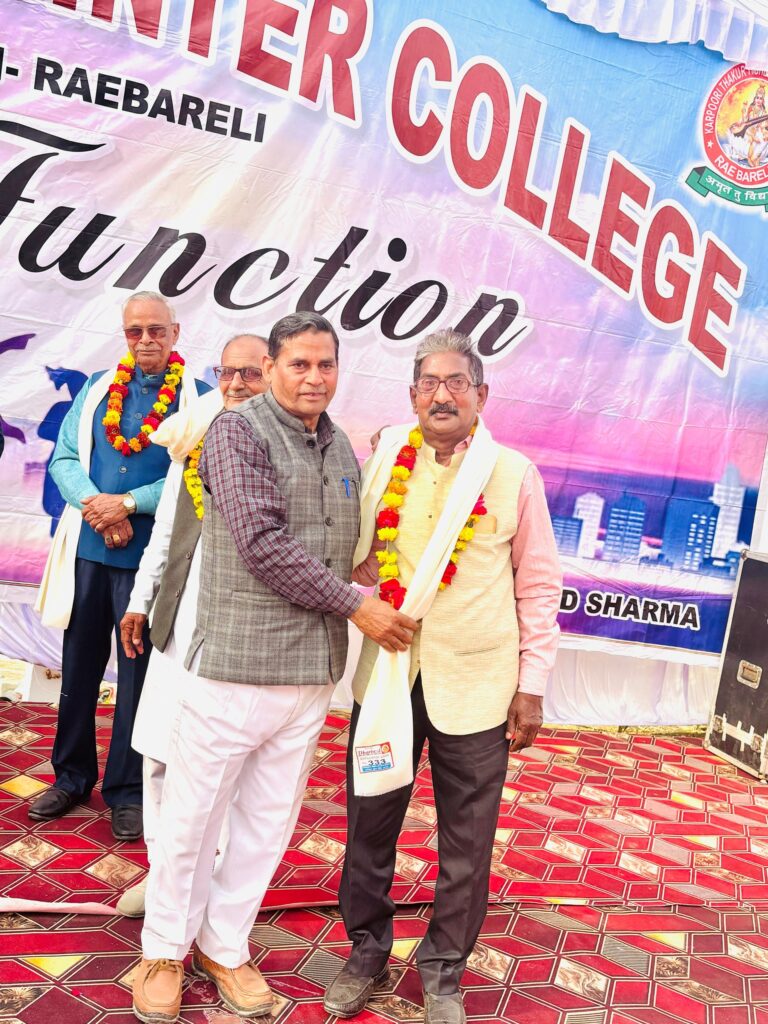 Senior invited guests wearing marigold garlands and ceremonial shawls standing together in front of the Annual Function banner.