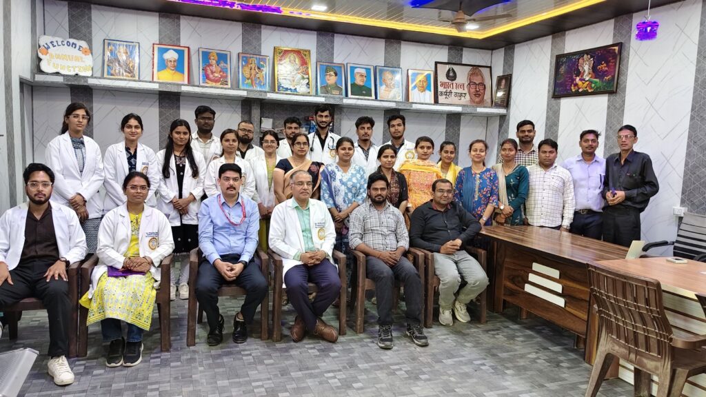 Visiting team in white medical coats photographed with college staff and students beneath the portrait of Bharat Ratna Karpoori Thakur