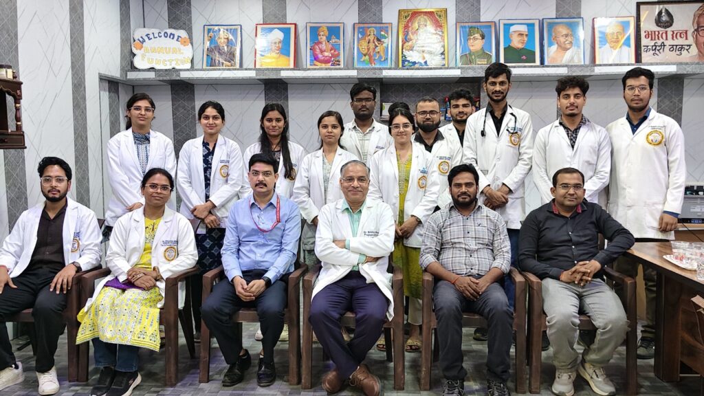 Visiting team in white medical coats seated with college staff for a group photograph in the college hall