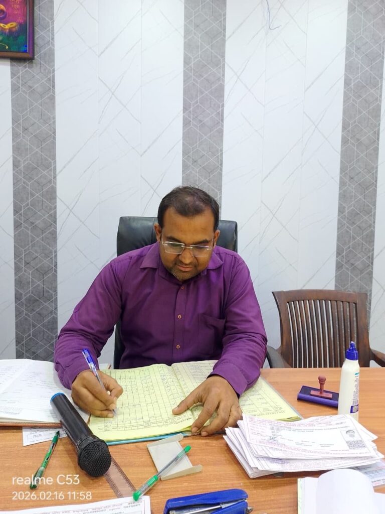 Principal Abhishek Srivastava writing in the school register at his desk in the college office.