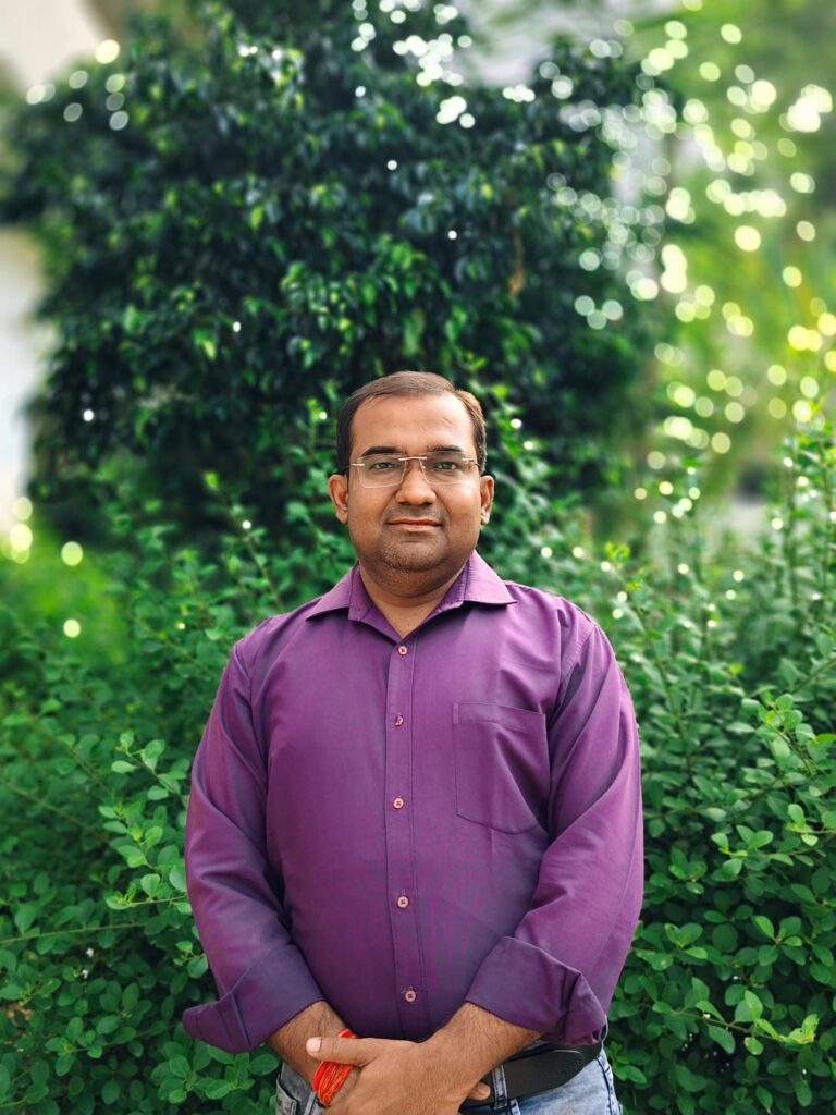 Portrait of Principal Abhishek Srivastava standing in front of greenery on the college campus.
