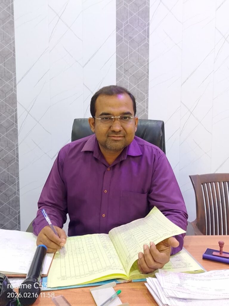 Principal Abhishek Srivastava seated at his desk with the school register open in front of him.