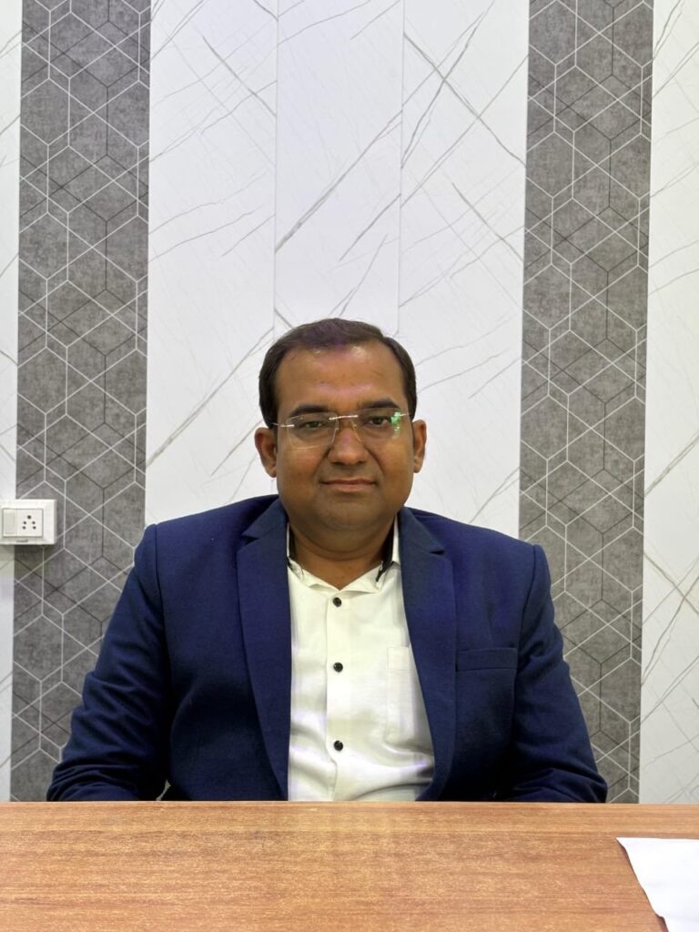 Principal Abhishek Srivastava seated at his office desk in a formal blazer.