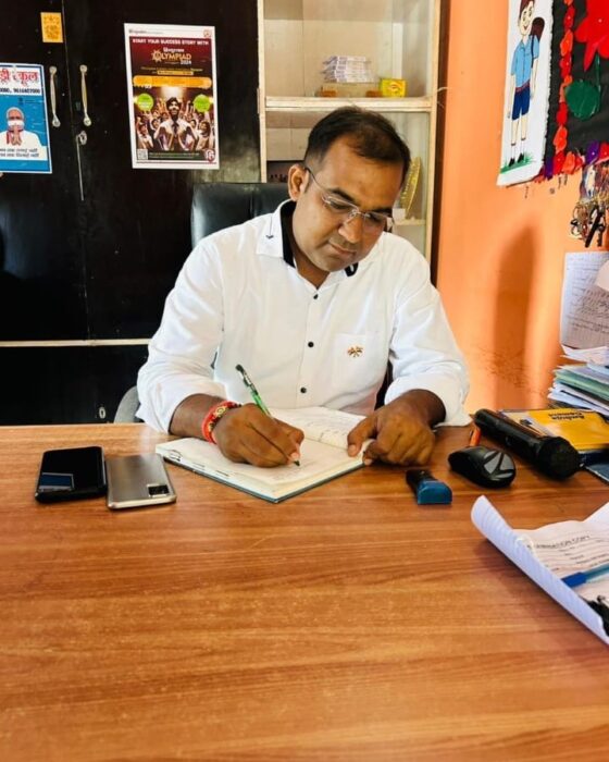Principal Abhishek Srivastava seated at a wooden desk in the office, signing the day's records.