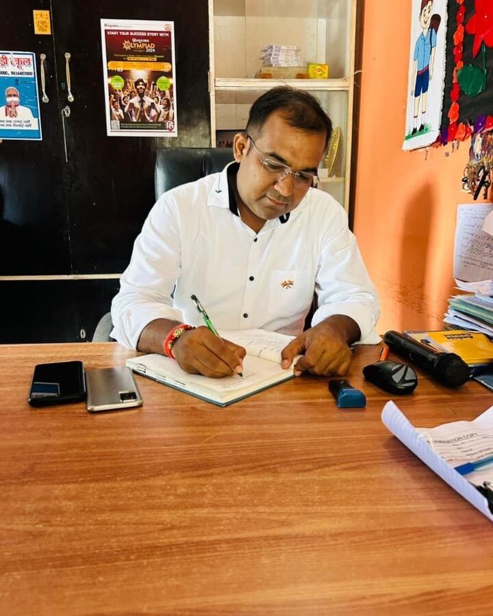 Principal Abhishek Srivastava seated at a wooden desk in the office, signing the day's records.