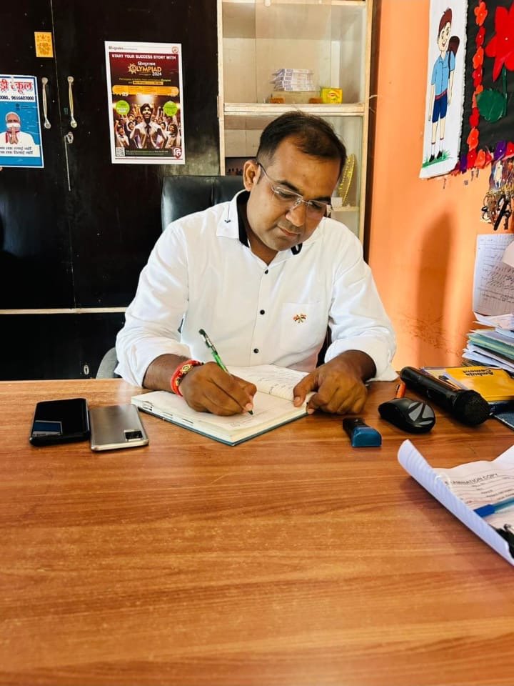 Principal Abhishek Srivastava seated at a wooden desk in the office, signing the day's records.