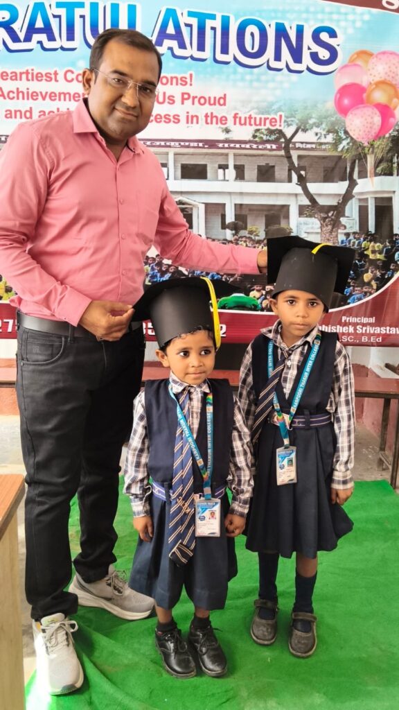 Principal Abhishek Srivastava standing with two nursery children wearing black graduation caps in front of a congratulations banner.
