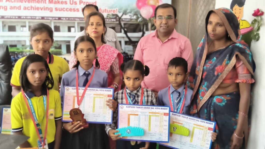 A group of primary-section students holding progress report cards and trophies, standing with their parents and teachers in front of a congratulations banner.