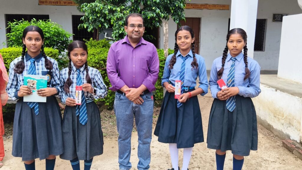 Four girls in school uniform holding small prizes and books, standing on either side of a teacher outside the college building.