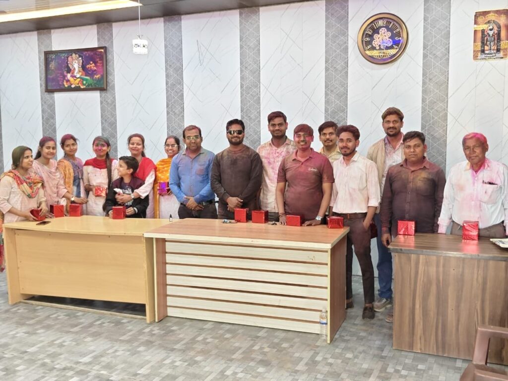 The college staff standing together in the office at Holi, with wrapped red gift boxes laid out on the desks in front of them.