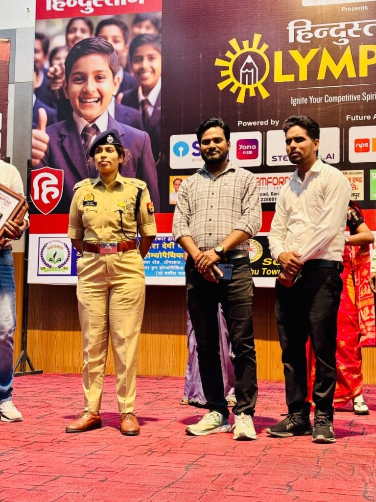 School staff on stage with a police officer in front of the Hindustan Olympiad backdrop