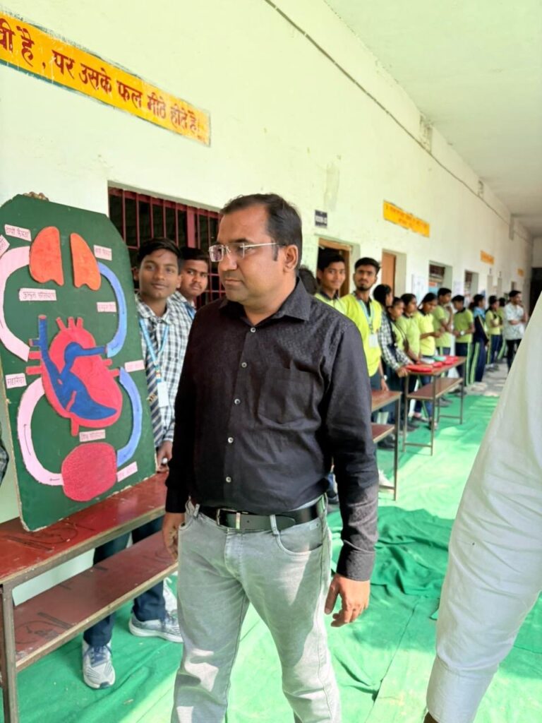 A teacher beside a hand-painted heart and circulation chart, with students lining the corridor exhibition behind him