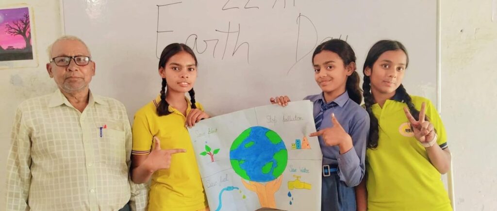 Three students holding a hand-drawn Earth Day poster about saving water, saving plants and stopping pollution, with a teacher beside them