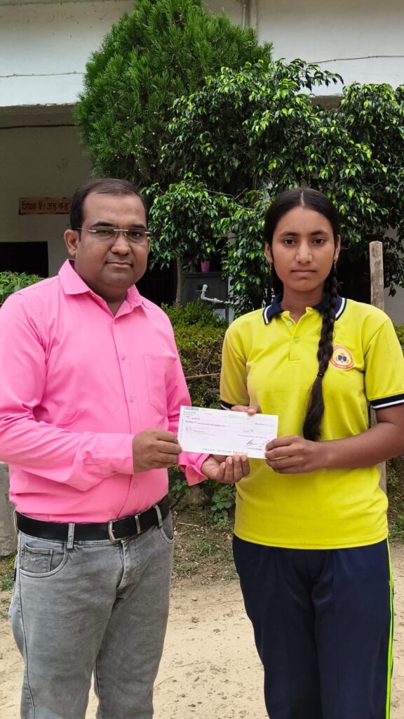 Principal Abhishek Srivastava handing a prize cheque to a student in the college's yellow sports kit, outside the school building.