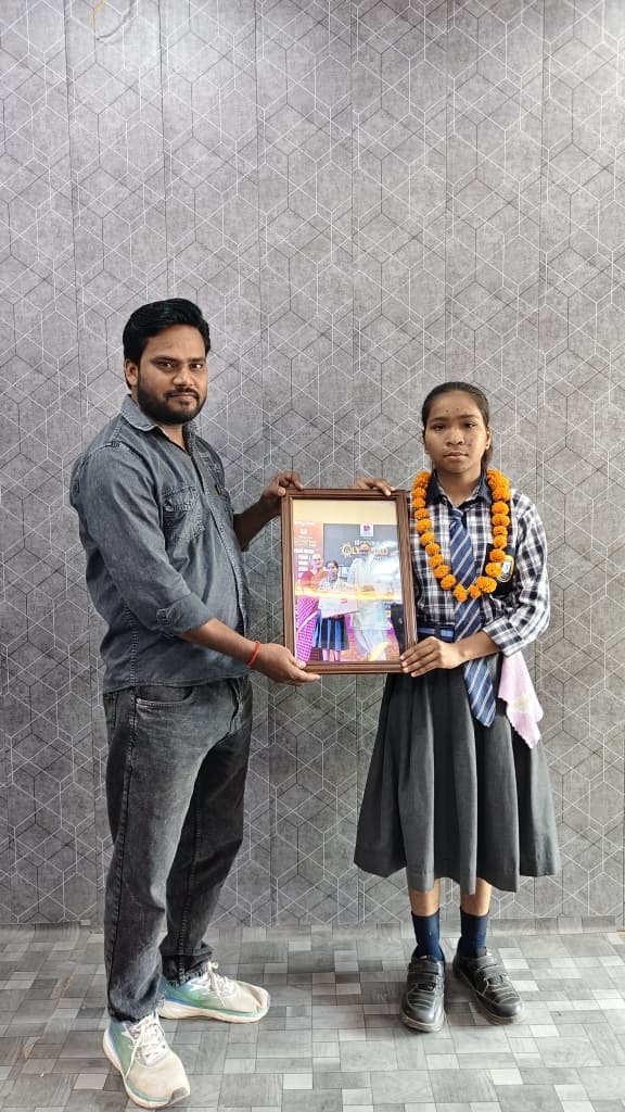 Manager Hariom Sharma presenting a framed photograph to a garlanded student in school uniform.