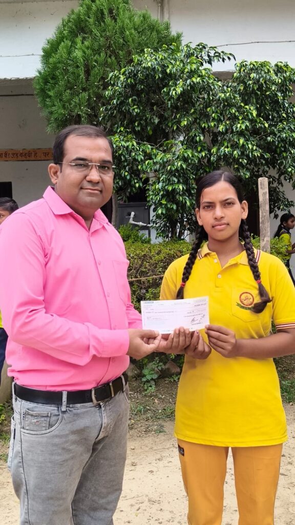Principal Abhishek Srivastava handing a prize cheque to a student in the college's yellow sports kit, with the school building behind them.