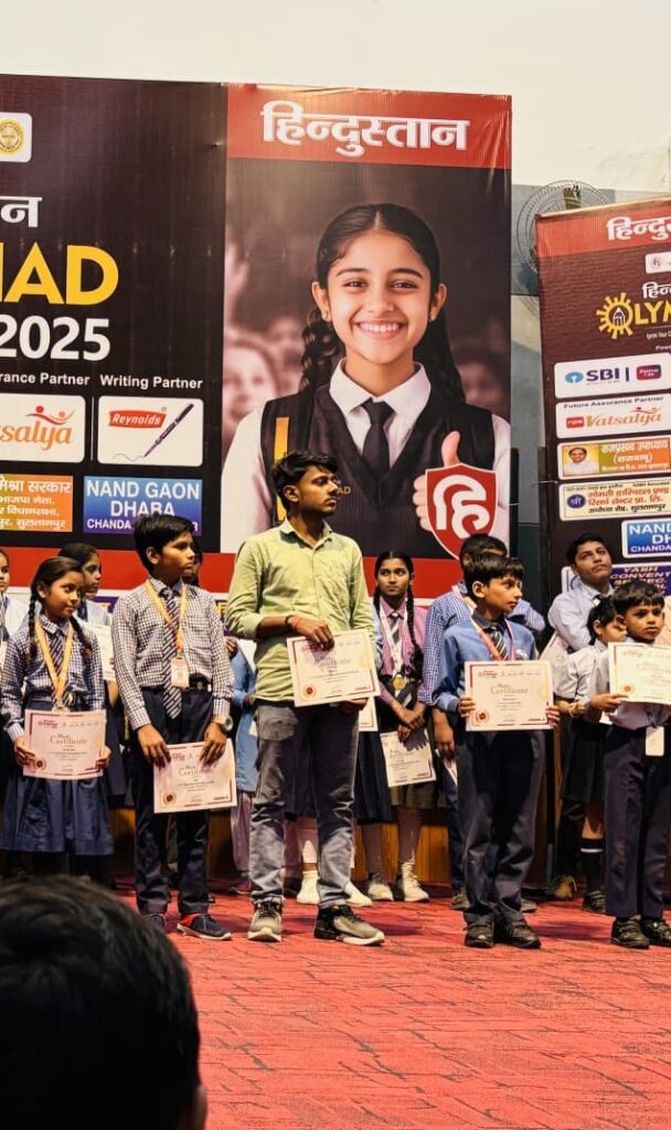 A row of school students holding Hindustan Olympiad 2025 merit certificates on stage at the award ceremony